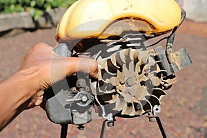 Flywheel of a small petrol engine used on a brush cutter held in the hand. Petrol tank and carburetor parts of gasoline grass