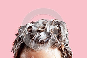 Fmale hair shampoo and foam on pink background close-up.