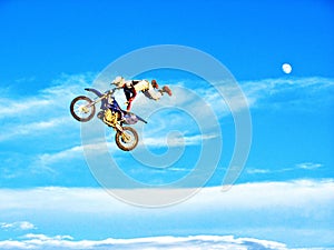 FMX motorbike rider completing stunts against the backdrop of a blue sky with clouds and the moon