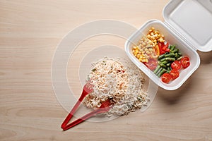 Foam plastic container with delicious food on wooden background