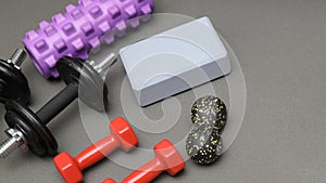 Foam rollers, dumbbells and yoga block on grey mat with massage roller. Set of fitness equipment on a gray background, front view