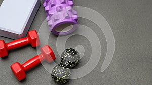 Foam rollers, dumbbells and yoga block on grey mat with massage roller. Set of fitness equipment on a gray background, front view