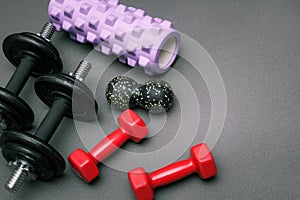 Foam rollers, dumbbells and yoga block on grey mat with massage roller. Set of fitness equipment on a gray background, front view