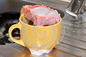 A foam sponge with detergent lies on a dirty cup, on the background of a washcloth, close-up.