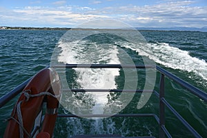 Foam trace in the water behind tourist, passenger catamaran sailing through the Lake Constance.