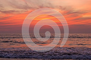 Foam of the waves of the sea against the backdrop of bright purple and orange sunset sky