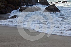 Foaming breaking wave and backwash foam on a sandy shoreline over boulders