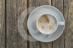 Foaming espresso with milk in white ceramic cup on a saucer stands on a wooden table. Coffee is aromatic and tasty drink photo
