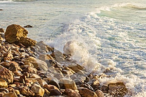 Foaming pastel wave washing across bay with distant wave backwash, breaking on rocky shoreline