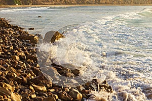Foaming pastel wave washing across bay with distant wave backwash, breaking on rocky shoreline