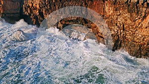 Foaming sea waves hitting rocky shore with splashes aerial view. Dangerous ocean