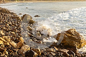 Foaming wave breaking at sunrise with rocky shoreline