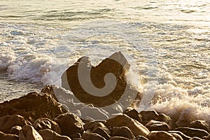 Foaming wave breaking at sunrise with rocky shoreline