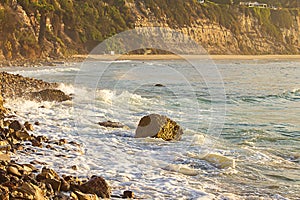 Foaming wave breaking at sunrise with rocky shoreline