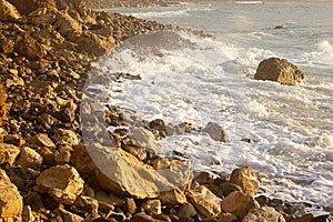 Foaming wave breaking at sunrise with rocky shoreline
