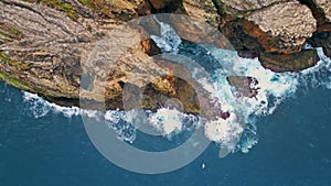 Foaming waves crashing rocky cliffs top view. Drone shot of dramatic coastline