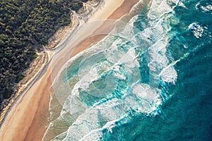 Foamy ocean waves roll and approach sandy beach. Majesty turquoise seascape. Top view from a drone