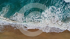 Foamy ocean waves rolling and coming on a sand beach. Sea or ocean surf wave. Aerial top down shot, 4K