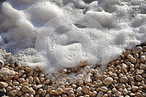 Foamy sea water splashing against rocks on the pebbles beach, closeup.Surf and pebbles