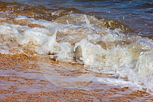 Foamy sea wave rolls over the sandy shore of the beach on a summer sunny day.