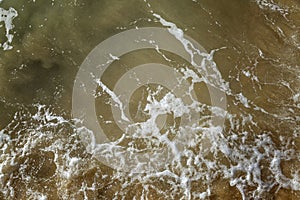 Foamy sea wave on the sandy shore. Muddy dirty green water surface. Top view. Background. Space for text