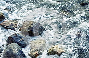 Foamy sea waves on large rocks on the shore. Close-up. Background. Space for text