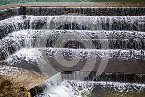 Foamy vertical water curtains falling over tiered concrete face.