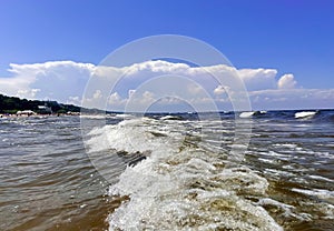 Foamy waves in the Baltic Sea against the blue sky with fluffy clouds in Jurmala