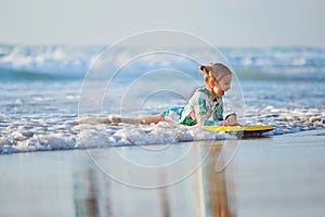 Foamy waves of the beautiful autumn sea splashing alongside a charming little girl on surfboard