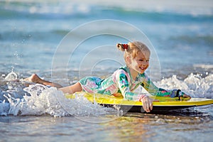 Foamy waves of the beautiful autumn sea splashing alongside a charming little girl on a yellow surfboard