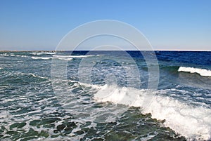 Foamy waves roll on the shore. In the distance the sea is bluer