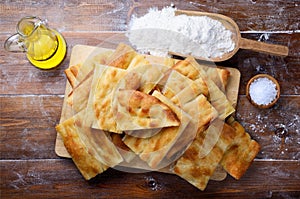 Focaccia bread, flatbread, with chopping board, olive oil, flour and salt on wooden floured background, Top view photo