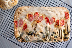 Focaccia garden, decorated with chives, basil and tomatoes, cooling on a wire tray.