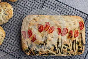 Focaccia garden, decorated with chives, basil and tomatoes, cooling on a wire tray.