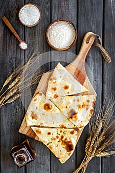 Focaccia ingredients. Wheat ears, flour, oil near bread on dark wooden background top-down