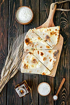 Focaccia ingredients. Wheat ears, flour, oil near bread on dark wooden background top-down