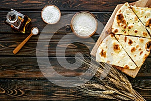 Focaccia ingredients. Wheat ears, flour, oil near bread on dark wooden background top-down copy space