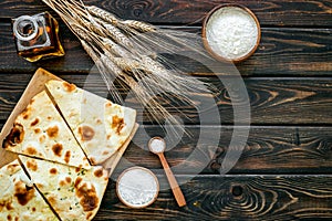 Focaccia ingredients. Wheat ears, flour, oil near bread on dark wooden background top-down copy space