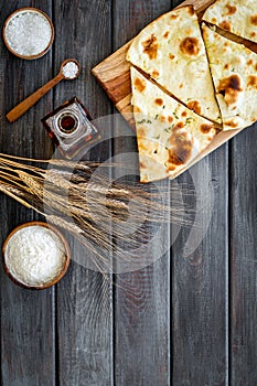 Focaccia ingredients. Wheat ears, flour, oil near bread on dark wooden background top-down copy space