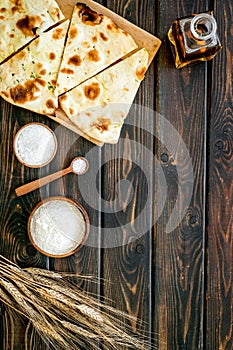 Focaccia ingredients. Wheat ears, flour, oil near bread on dark wooden background top-down copy space