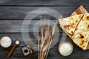 Focaccia ingredients. Wheat ears, flour, oil near bread on dark wooden background top-down copy space