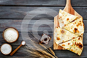 Focaccia ingredients. Wheat ears, flour, oil near bread on dark wooden background top-down copy space