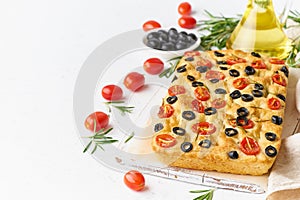 Focaccia with tomatoes, olives and rosemary, copy space, side view. Whole Italian flat bread, bottle with oil