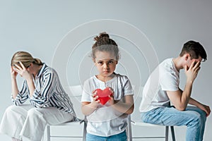 Focus of adopted african american kid holding red heart near divorced foster parents on grey photo