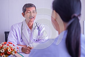 Focus of Asian mature male doctor and female patient sitting talking in hospital.