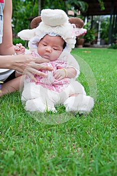 Focus at Asian newborn baby girl with costumes little sheep in the garden and mother is holding her.