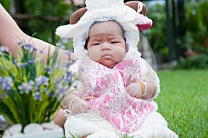 Focus at Asian newborn baby girl with costumes little sheep in the garden and mother is holding her.