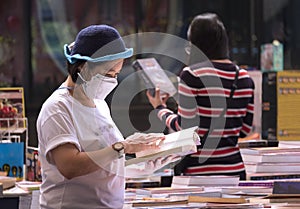 Focus at Asian plus size woman in protective face mask choosing books at bookstore in shopping mall