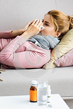 Focus of attractive and ill woman with grey scarf sneezing and using napkin