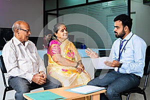 Focus on banker, Bank employee explaining about insurance or loan policy to senior couple at office - concept of